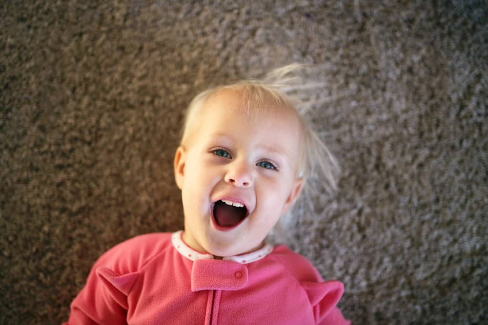 Toddler lying on carpet and laughing—parents consider how many words should an 18 month old say