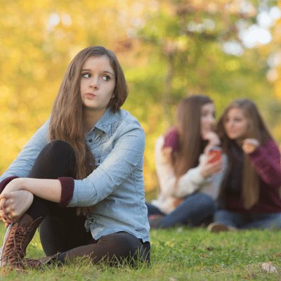 A teen sits alone while peers gossip, reflecting effects of sudden stuttering in teenager socially