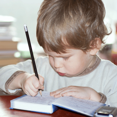 Young boy concentrates on writing in a notebook, practicing fine motor skills and handwriting