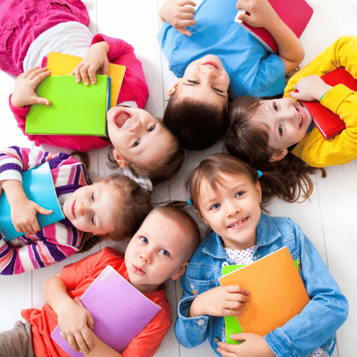 Group of smiling children lying in a circle with colorful books, showing joy in learning