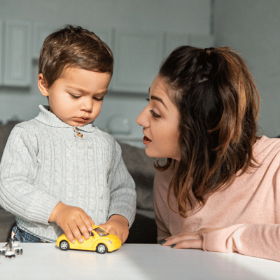 Mother talks to toddler playing with a yellow toy car to encourage speech and engagement