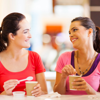 Two smiling teenage girls enjoy ice cream indoors, showing positive communication and friendship through conversation