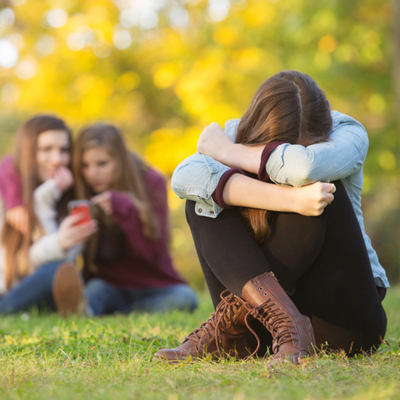 A sad teenage girl sits on the grass, highlighting conversation skills for teens dealing with bullying