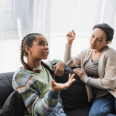 Parent listens attentively as daughter explains feelings, gesturing animatedly during supportive living room conversation time