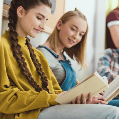 Two teenage girls read books in hallway, illustrating why is figurative language important in education