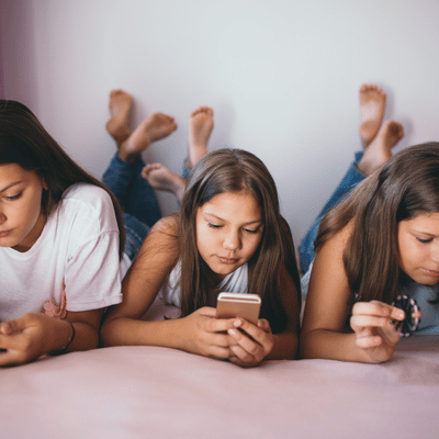 Photo shows girls lying on bed using phones, highlighting speech therapy services and social skills