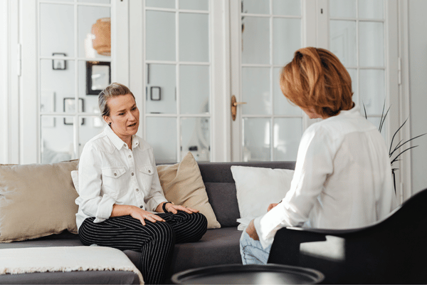 Two adult women discuss concerns during private speech therapy session in a calm living-room setting