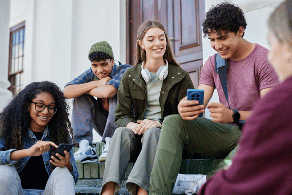 Photo shows teens sitting on steps using smartphones, relating to speech therapy services for communication
