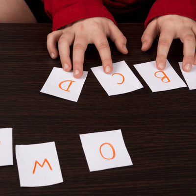 Small hands arrange alphabet cards on table during pediatric speech therapy, building early phonics skills
