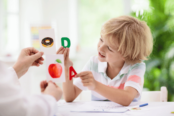 Child matches letter cards with pictures during pediatric speech therapy activity at table with therapist