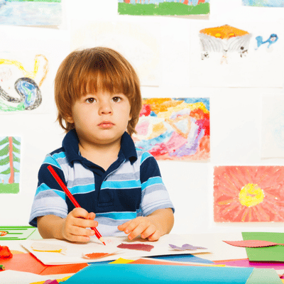 Young child draws with crayons at table, practicing focus before speech therapist for 2-year-old sessions