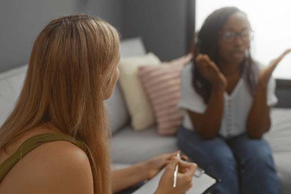 Counselor takes notes while client speaks on couch, showing benefits of speech therapy for adults