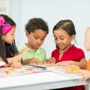 Four young children gather around a table and look at a colorful learning activity together in a bright classroom setting