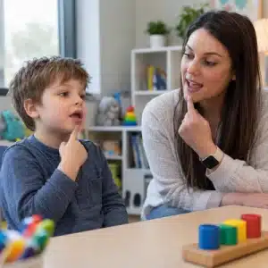 A speech-language pathologist and young child use visual mouth cues while practicing sounds during therapy for apraxia of speech in children